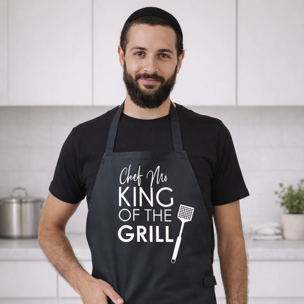 Man wearing a black apron with 'King of the Grill' text in a kitchen setting